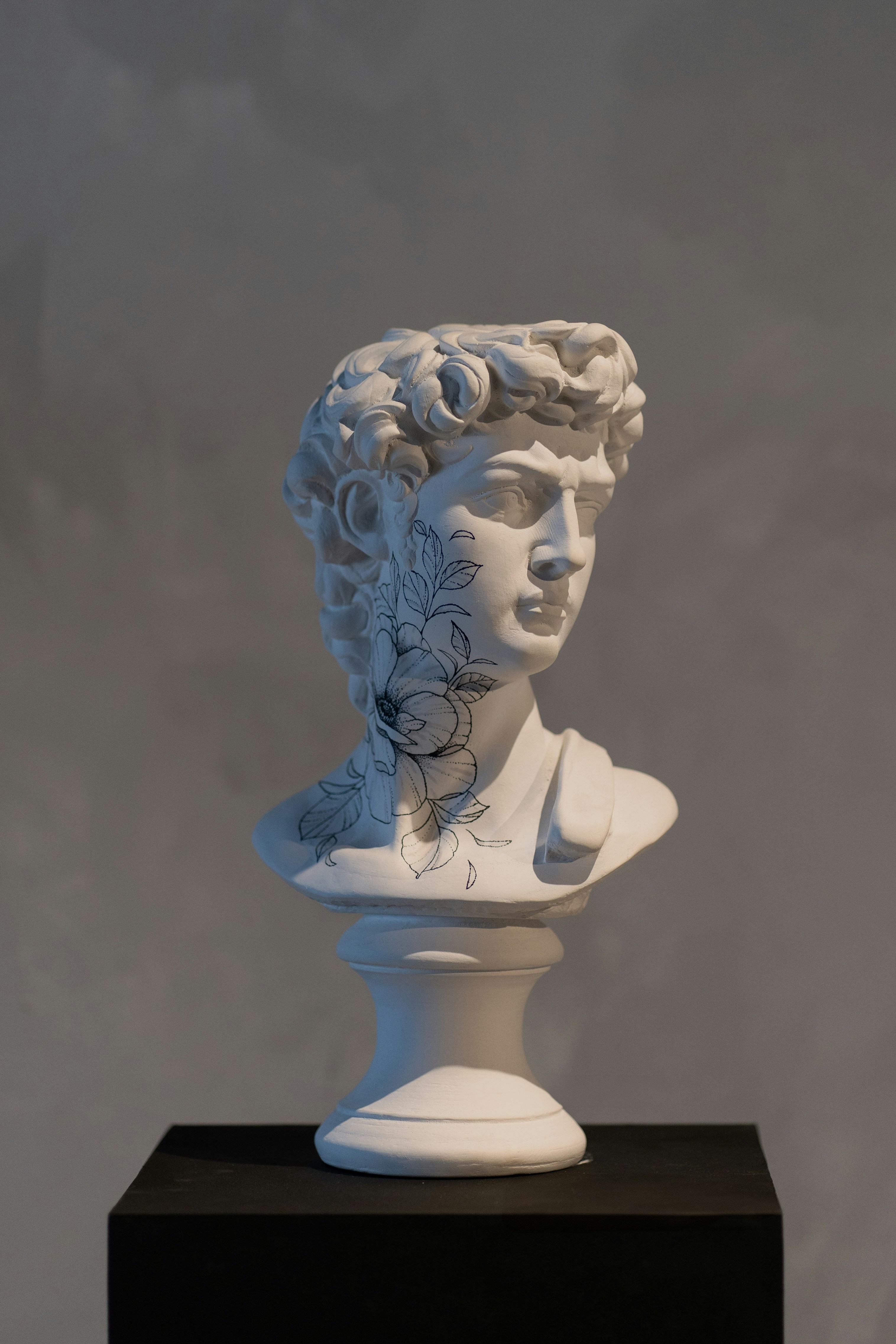 A marble bust with a fine-line floral tattoo, ritual card