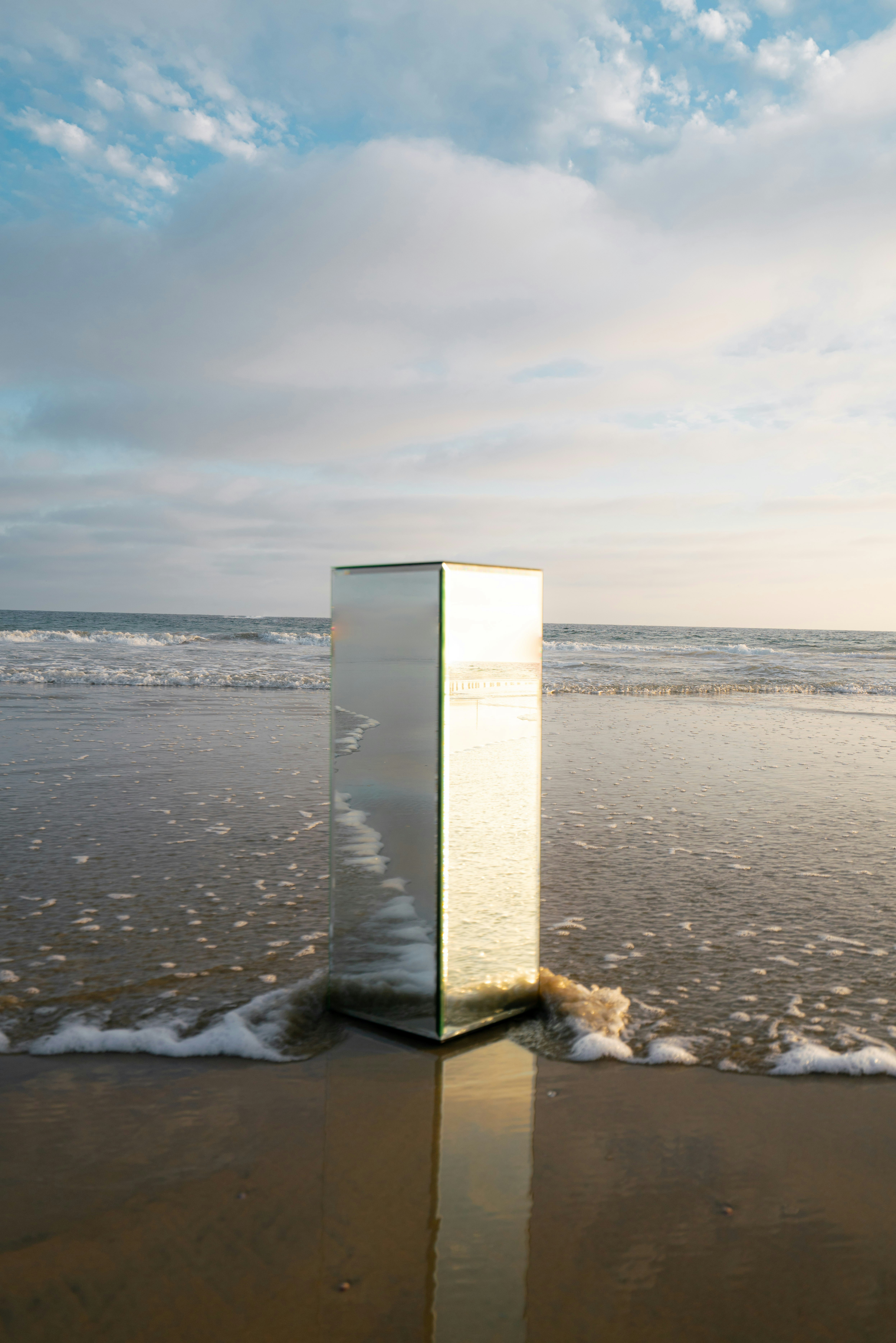 A mirrored monolith standing in shallow ocean waves